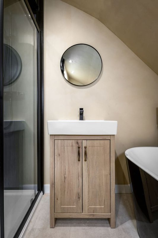 Modern bathroom with wooden vanity, white sink, round mirror and black freestanding bathtub