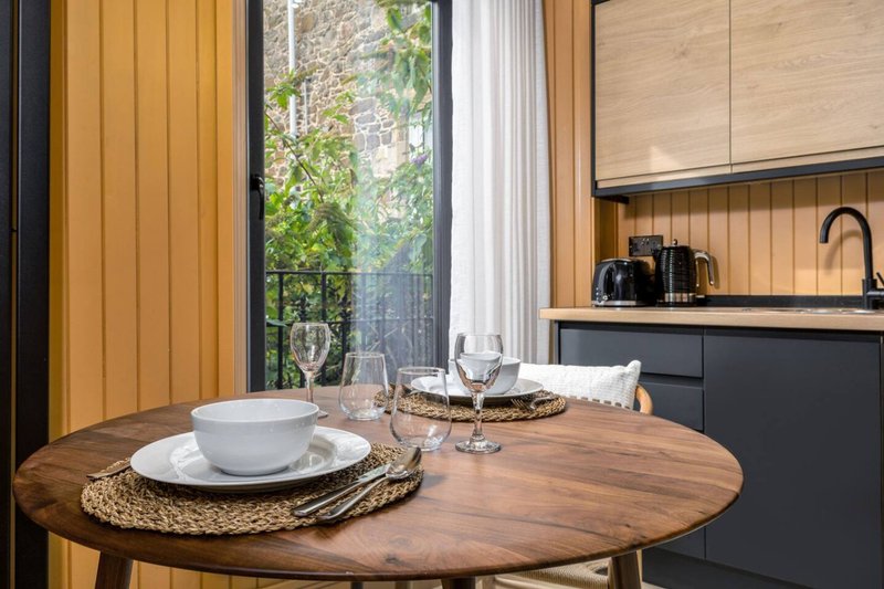 Modern dining area with round wooden table, place settings, and contemporary kitchen visible through opening