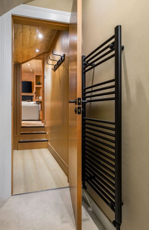 Narrow hallway with wooden door, black towel radiator and light flooring