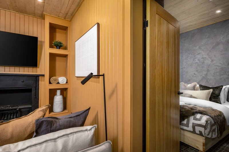 Modern bedroom interior with wooden paneling, fireplace, bed with patterned bedding, and wall-mounted lamp
