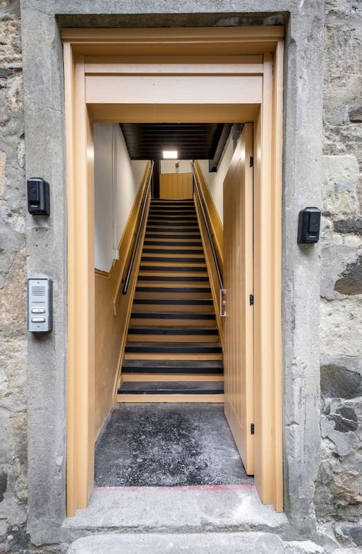 Entrance hallway with wooden staircase leading upward, stone walls, and wall-mounted lighting fixtures