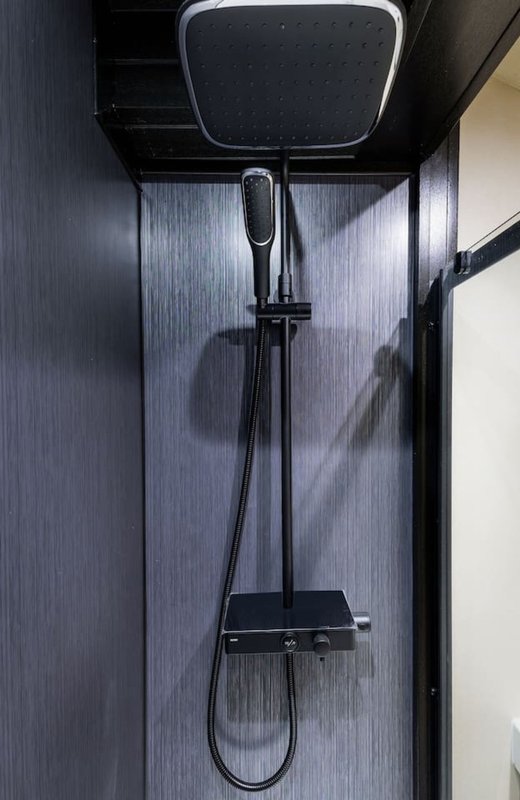 Modern shower enclosure with black fixtures, square rainfall showerhead and vertical tile walls