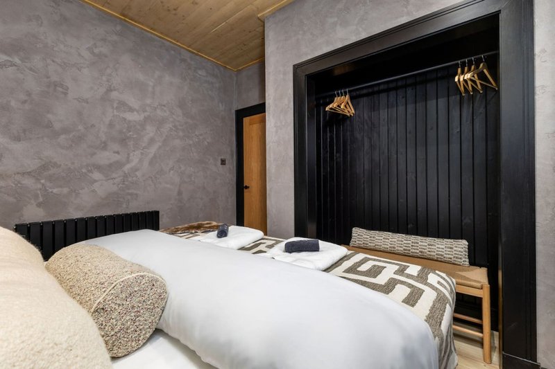 Modern bedroom with double bed, black headboard, textured walls, wooden ceiling and wardrobe