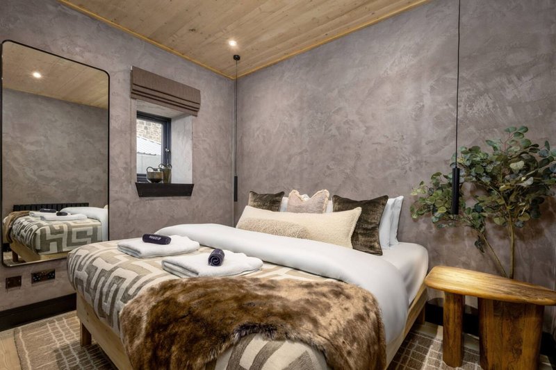 Modern bedroom with double bed, fur throw, white pillows, grey textured walls and wooden ceiling