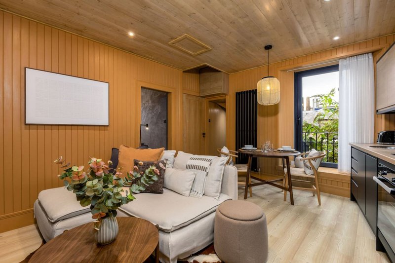 Warm wooden open-plan living area with cream sofa, dining table, kitchenette and garden views