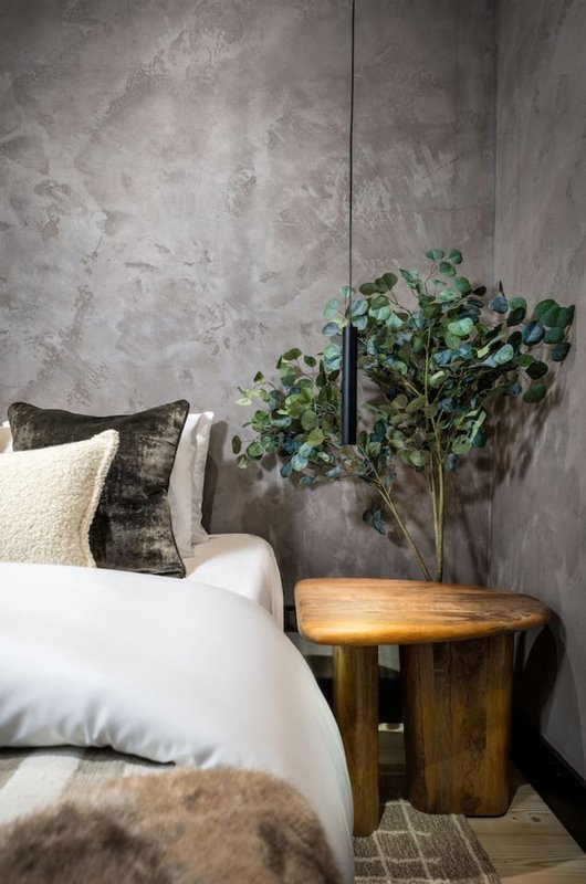 Bedroom with white pillows, wooden side table, potted plant, and textured grey wall