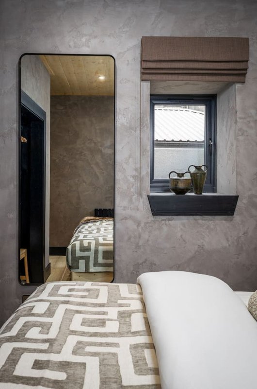 Modern bedroom with geometric patterned bedding, large mirror, window with brown valance and shelf