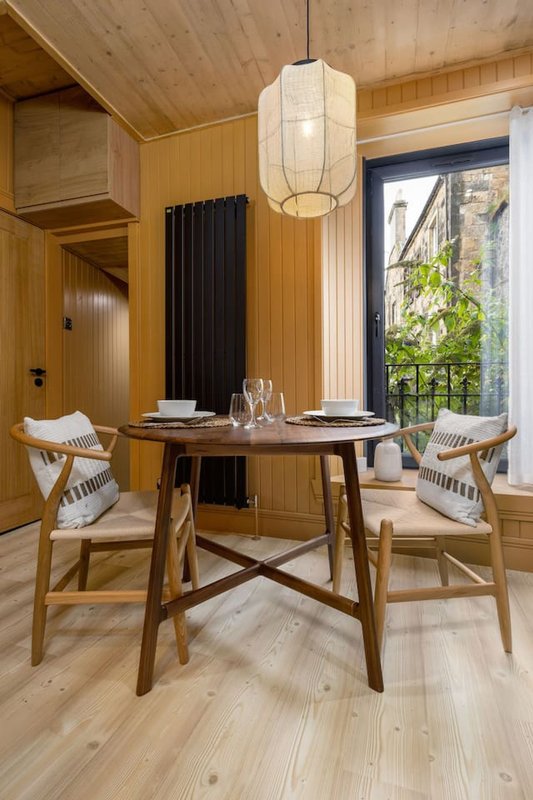 Modern dining room with round wooden table, two chairs, pendant light and large window with garden view