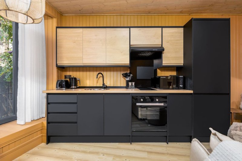 Modern kitchen with black cabinetry, wooden countertop, integrated oven, and light wood walls