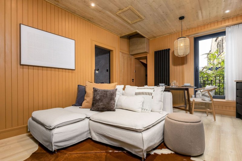 Modern lounge with cream L-shaped sofa, wooden walls, flat-screen TV and natural light