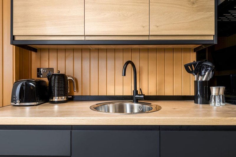 Modern kitchen with wooden backsplash, stainless steel sink, and black appliances