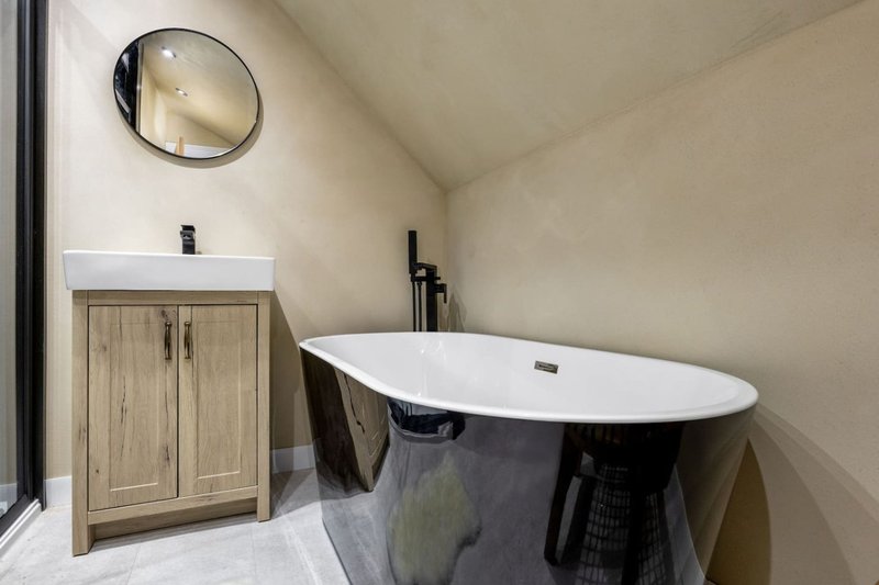 Modern bathroom with freestanding black bathtub, wooden vanity, round mirror and white sink
