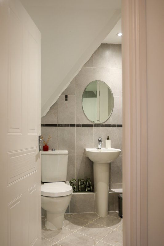 Modern bathroom with toilet, pedestal sink, round mirror and tiled walls