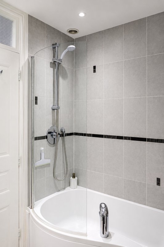 Modern bathroom with corner bathtub, glass shower enclosure, grey tile walls and recessed lighting