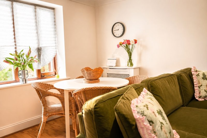 Bright living room with round table, rattan chair, green sofa, and potted plants by window