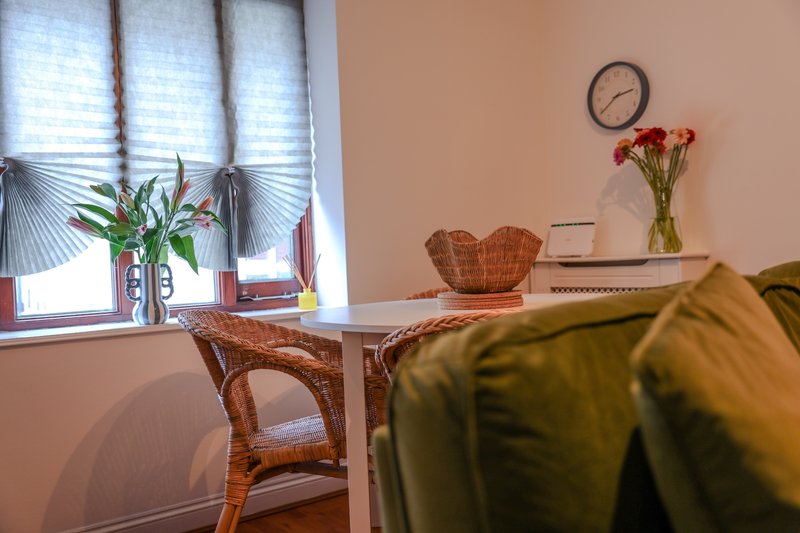 Cozy workspace with desk, wicker chair, window with blinds, plants and wall clock