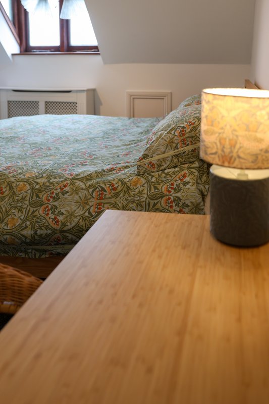 Bedroom with double bed, patterned bedding, wooden desk, table lamp and skylight window