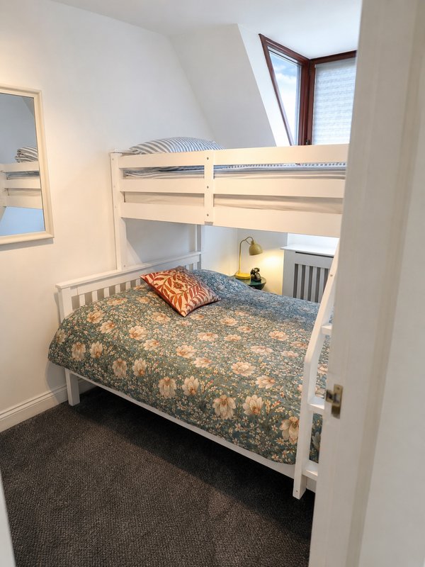 Bedroom with white bunk beds, patterned bedding, skylight window and dark carpet