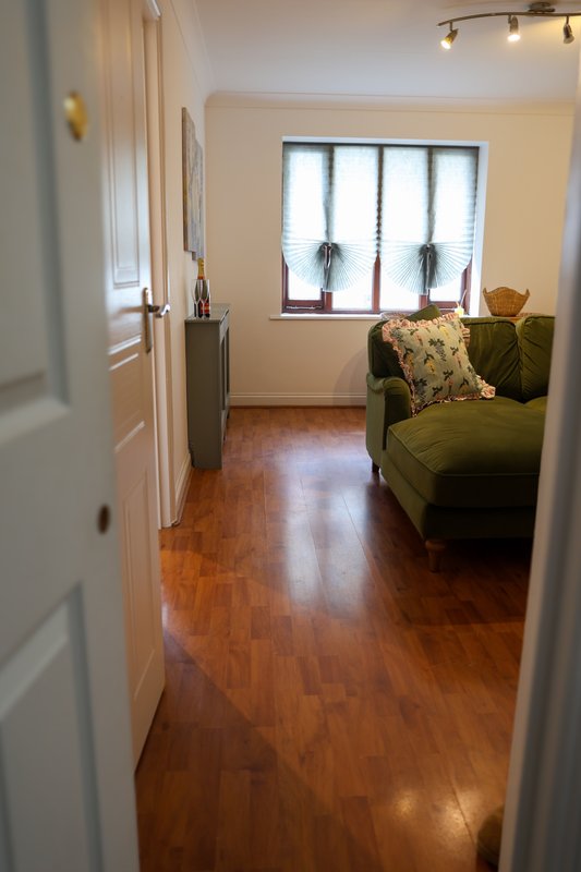 Hallway with wooden floor, white walls, green armchair and window with blinds.