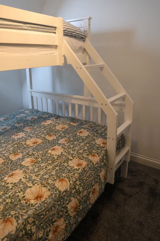 White wooden bunk bed with floral bedding and carpeted floor in bedroom
