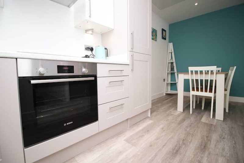 Modern kitchen with white cabinetry, black oven, and dining area with teal accent wall