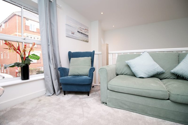 Modern living room with blue armchair, green sofa, large window and flowers