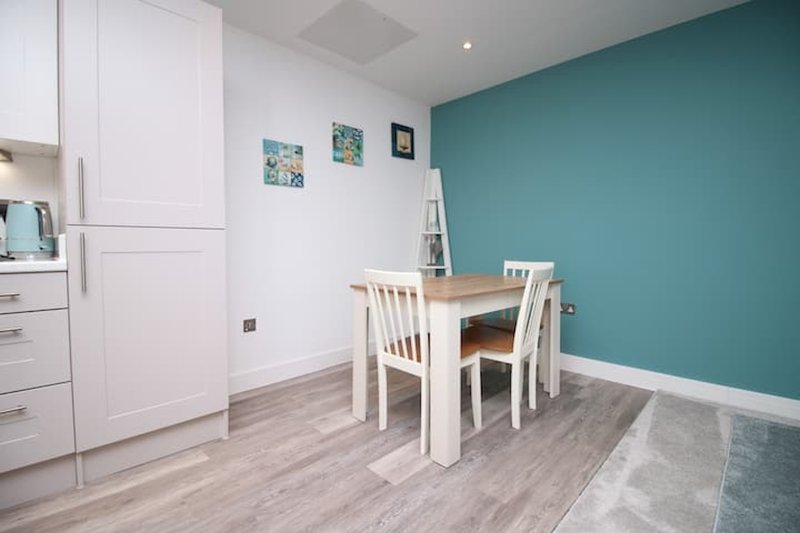 Modern kitchen-dining area with white cabinetry, teal accent wall, wooden table and chairs