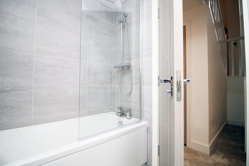 Modern bathroom with white bathtub, glass shower screen and grey tiled walls