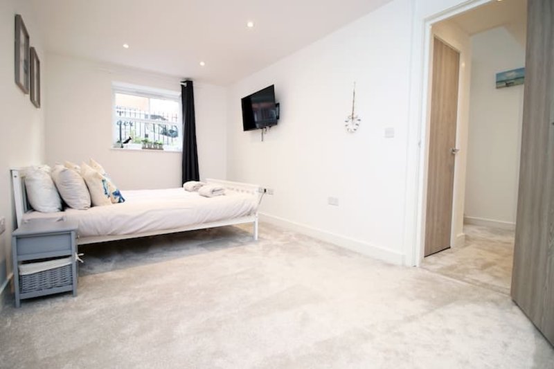 Spacious modern bedroom with double bed, light grey flooring, wall-mounted TV and en-suite doorway
