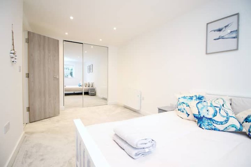 Bright modern bedroom with white bed, blue cushions, mirrored wardrobe and en-suite access