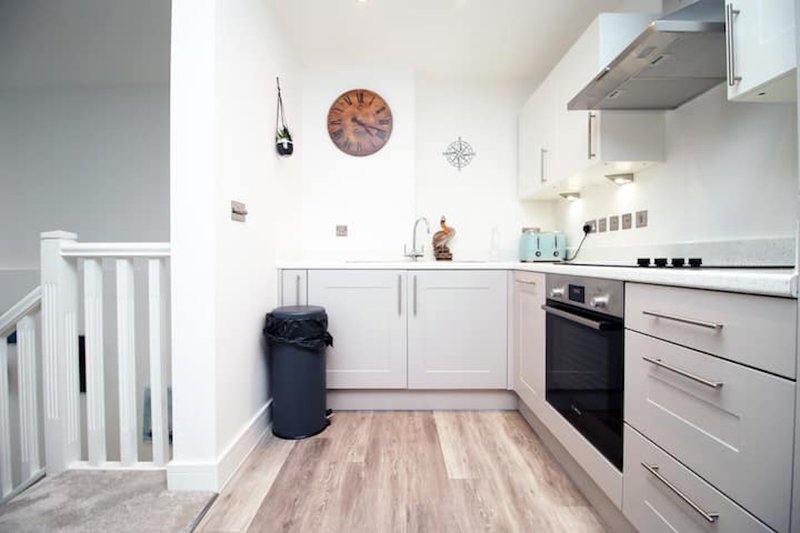 Modern kitchen with white cabinetry, black oven, wooden flooring and wall clock