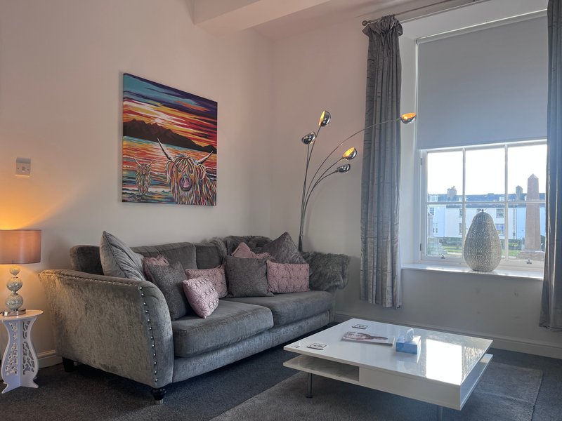 Modern living room with grey upholstered sofa, cushions, artwork, floor lamp and city view from window