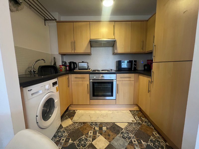 Modern kitchen with wooden cabinets, stainless steel appliances, washing machine and patterned flooring