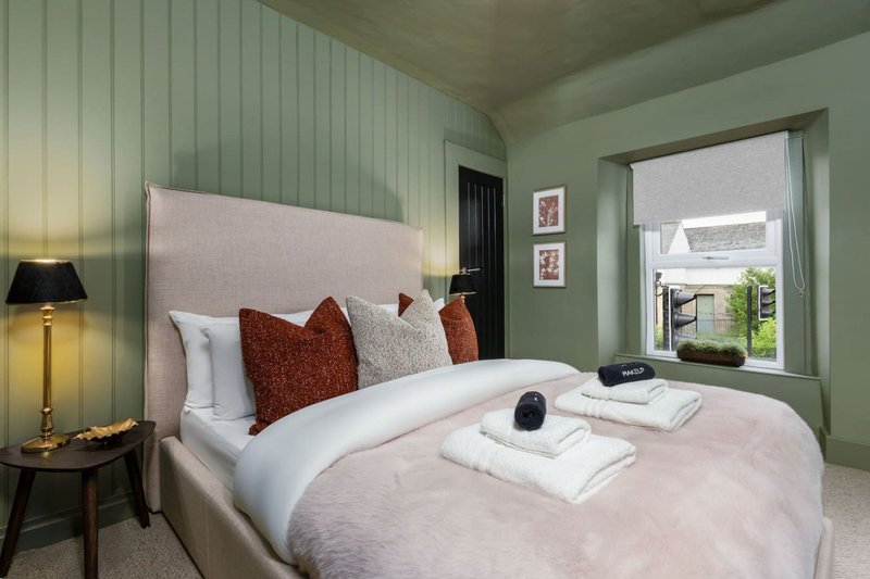 Modern bedroom with upholstered headboard, white bedding, rust and cream pillows, green walls and window