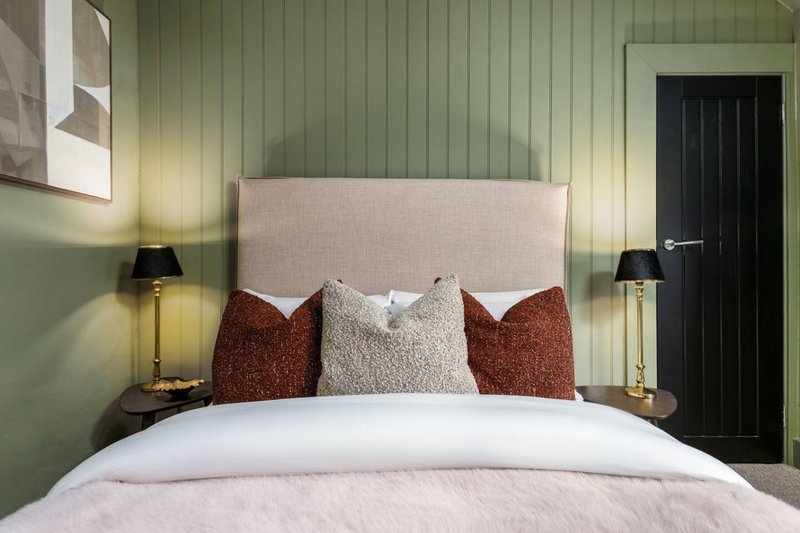 Bedroom with upholstered headboard, white bedding, decorative pillows, green walls and bedside lamps