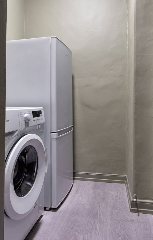 Laundry room with white washing machine and refrigerator against beige walls