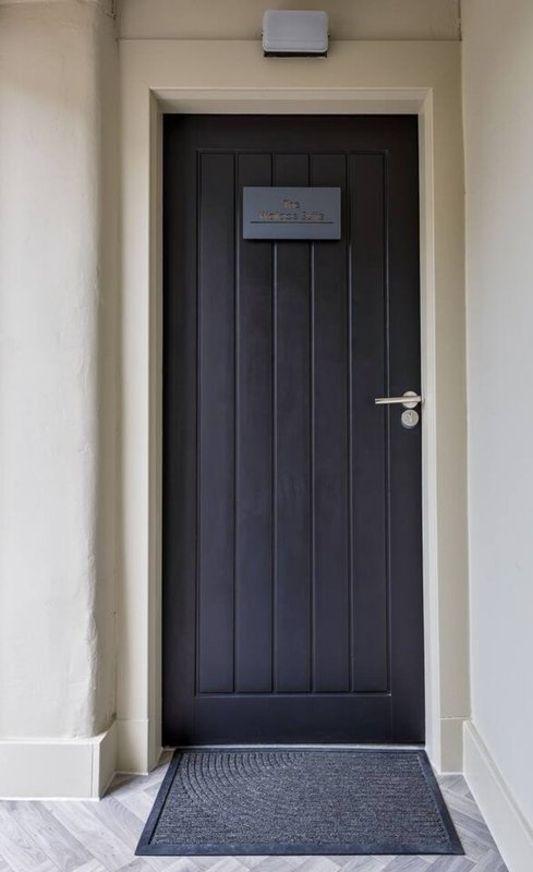 Black panelled front door with white frame, doormat and wall-mounted intercom