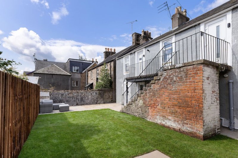 Rear garden with lawn, brick wall, metal railings and neighbouring stone properties