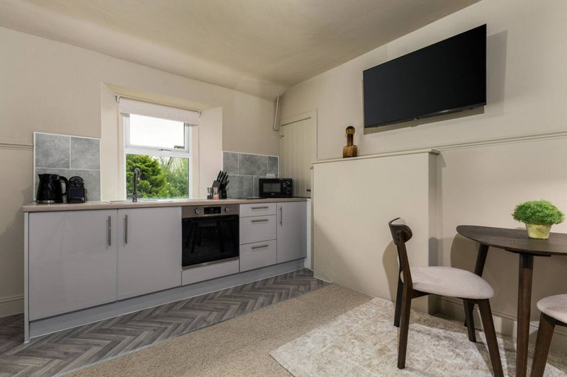 Modern kitchen and dining area with grey cabinetry, black oven, wall-mounted TV and small dining table