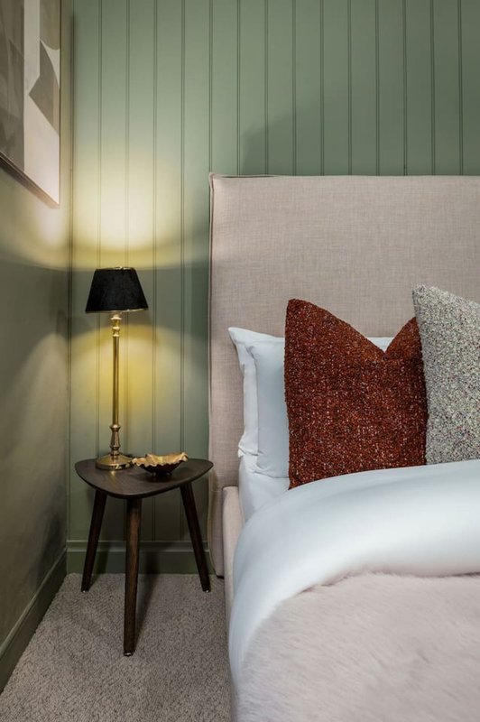 Bedroom with upholstered headboard, decorative pillows, bedside table lamp and green walls