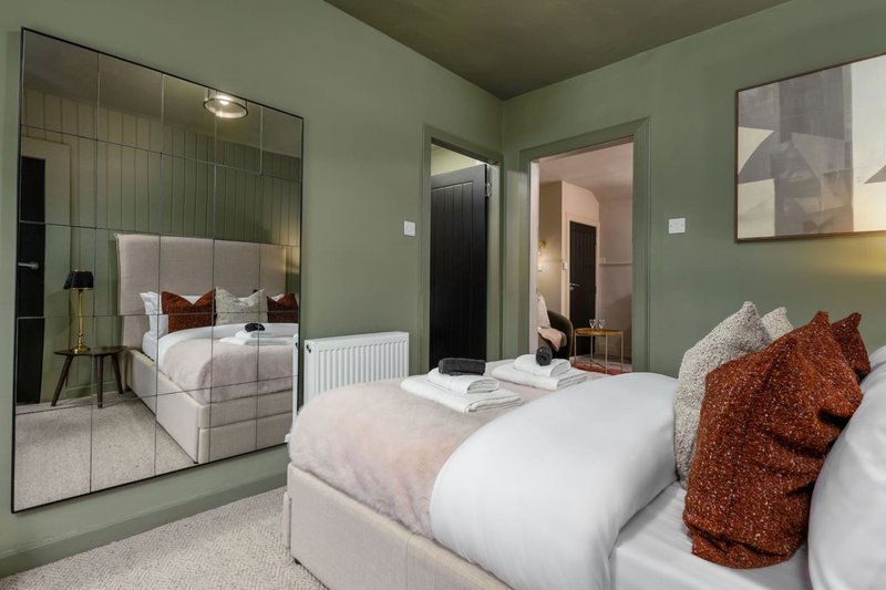 Modern bedroom with two beds, sage green walls, large mirror, and contemporary furnishings