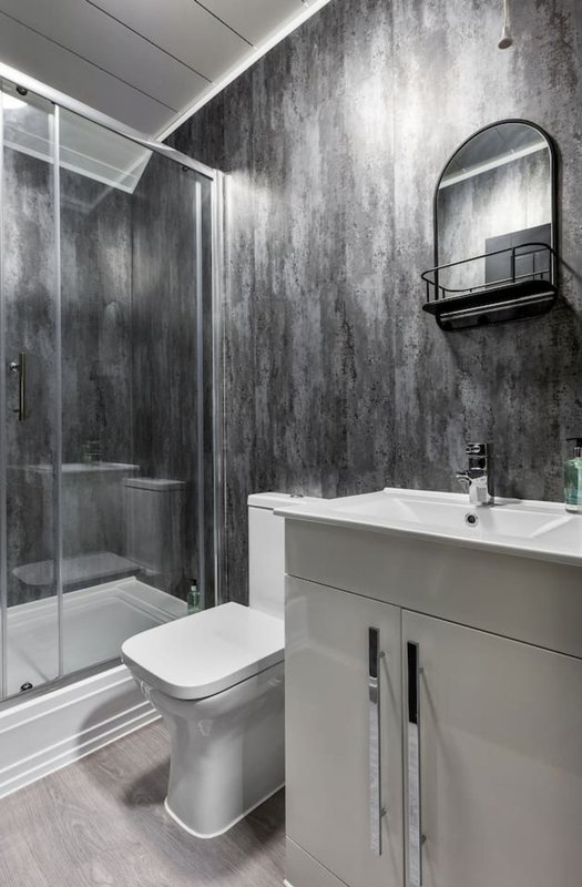 Modern bathroom with dark textured walls, white vanity, toilet, shower enclosure and mirror
