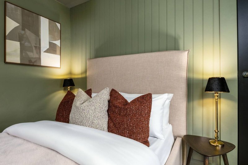 Modern bedroom with upholstered headboard, decorative pillows, white bedding, sage green walls and bedside lamps