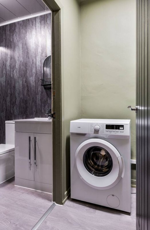 Utility room with white washing machine, sink vanity, and open bathroom doorway with shower