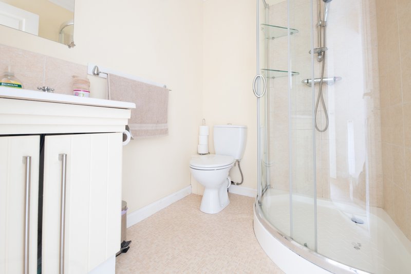 Modern bathroom with white vanity, toilet, corner shower enclosure and beige flooring