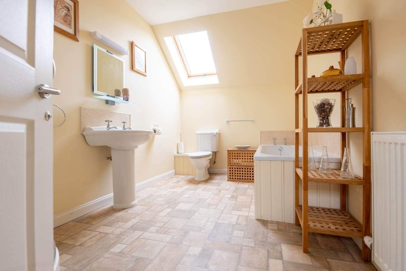 Bright bathroom with pedestal sink, toilet, wooden shelving unit and skylight