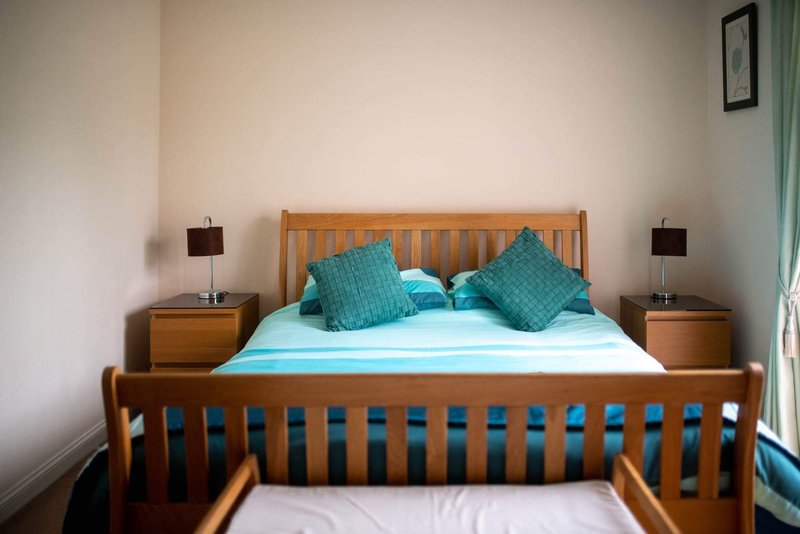 Bedroom with wooden double bed, turquoise bedding and pillows, wooden bedside tables and lamps