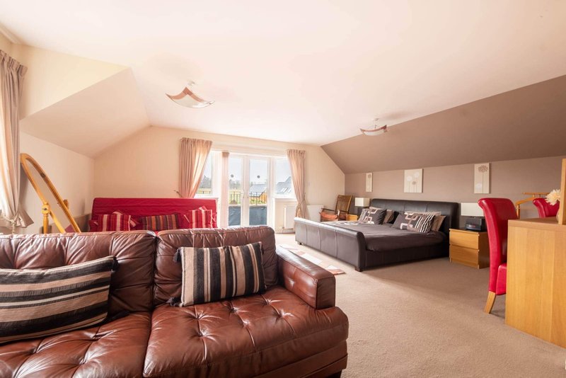 Large open-plan attic bedroom with leather sofas, double bed, and burgundy seating area