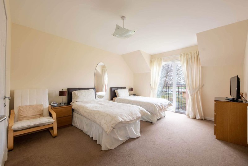 Spacious bedroom with two single beds, wooden furniture, large windows and cream décor