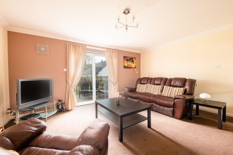Spacious living room with brown leather sofa, TV, coffee table and patio doors